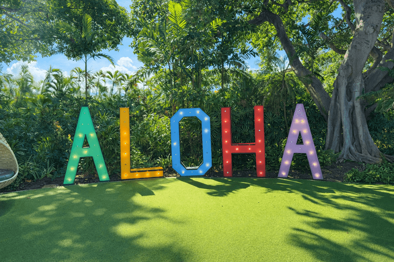 Ein farbenfrohes Aloha-Schild im Freien stellt die Bedeutung von Aloha in der hawaiianischen Sprache dar.