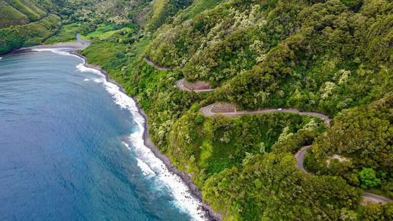 Aerial view of winding road along Maui coastline with ocean and green cliffs