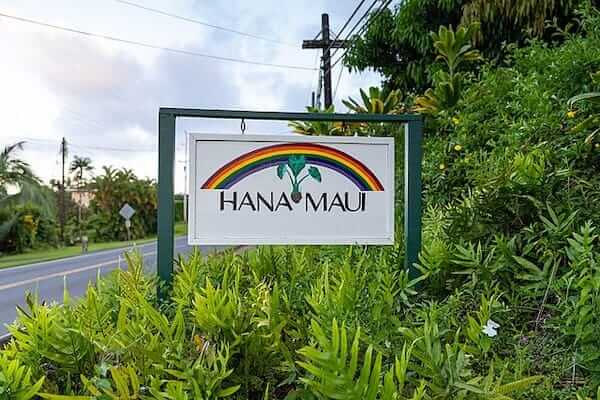 Hana Maui welcome sign with rainbow along roadside surrounded by greenery