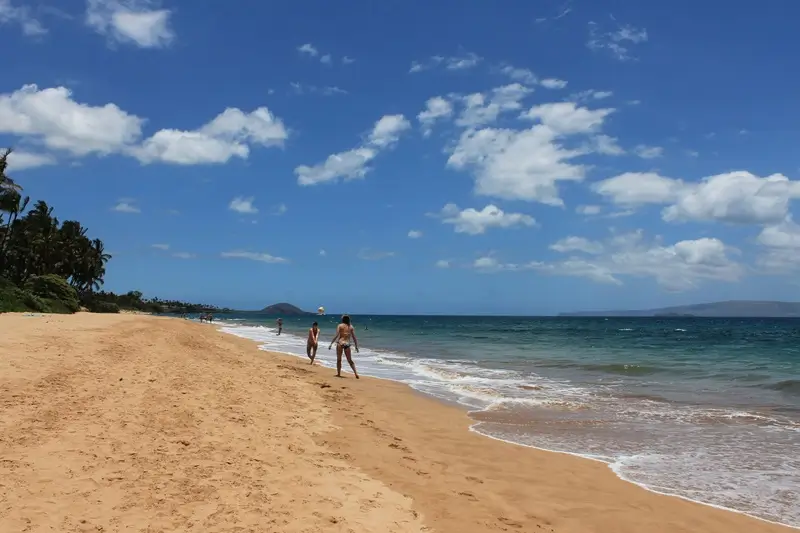 Keawakapu Beach, Maui, with a sandy shoreline, ocean waves, and people playing volleyball in the water