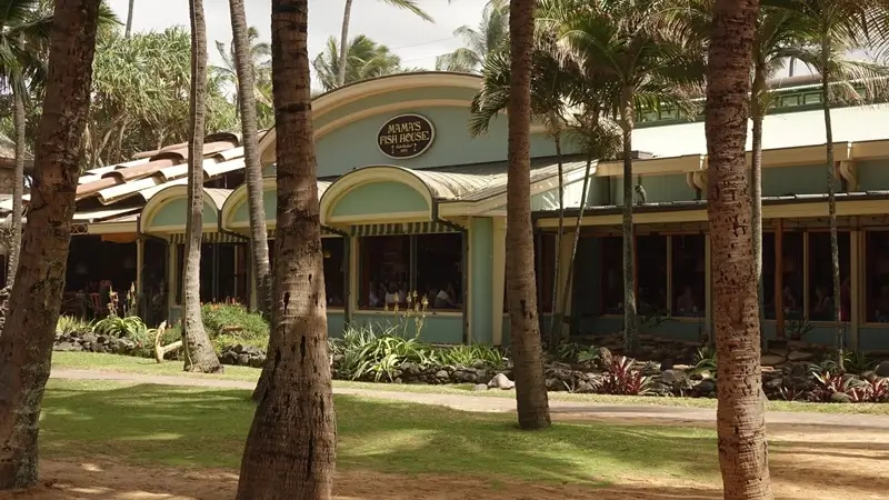 Vista exterior de Mama's Fish House en Maui, con palmeras, césped y el edificio del restaurante enmarcado por un paisaje tropical.