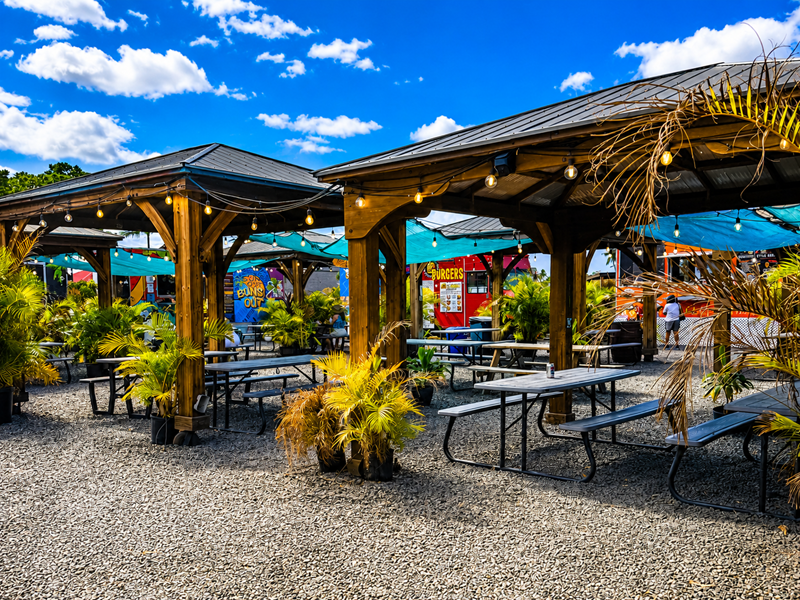 Outdoor seating area at Maui Food Trucks in Kihei, Maui, with picnic tables, string lights, and food trucks.