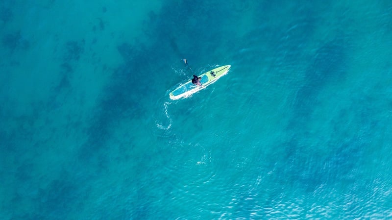Vista aérea de una persona practicando paddleboarding en aguas cristalinas de color turquesa durante una tranquila actividad acuática en Maui.