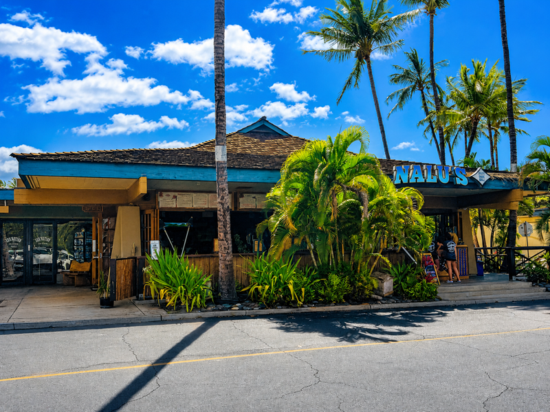 Außenansicht des Restaurants Nalu's South Shore Grill in Kihei, Maui, mit Palmen und tropischer Landschaftsgestaltung.