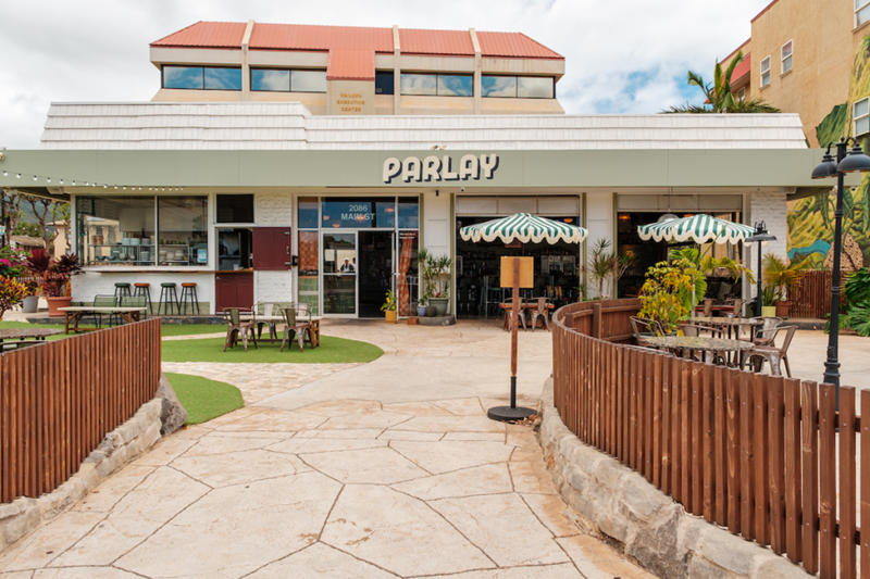 Parlay storefront in Wailuku, Maui with outdoor seating, striped umbrellas, wood fencing, and a courtyard walkway.