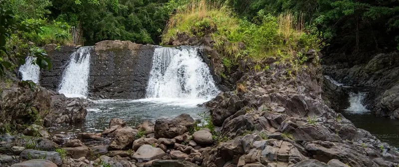 Waterfall flowing over rocky ledges into a pool surrounded by lush greenery along Pipiwai Trail Maui