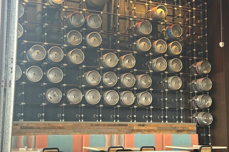 Interior of a brewery in Maui with beer kegs displayed on a wall above dining tables.