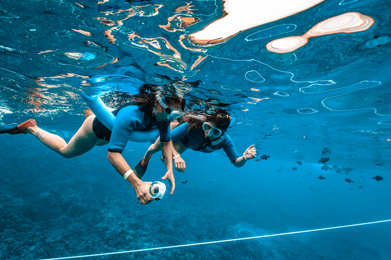 Two snorkelers using an underwater camera for Maui snorkeling photography in clear blue water