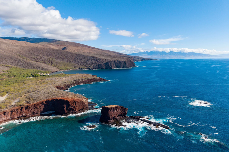 Rugged Lānaʻi coastline beside deep blue Pacific waters with a neighboring Hawaiian island in the distance
