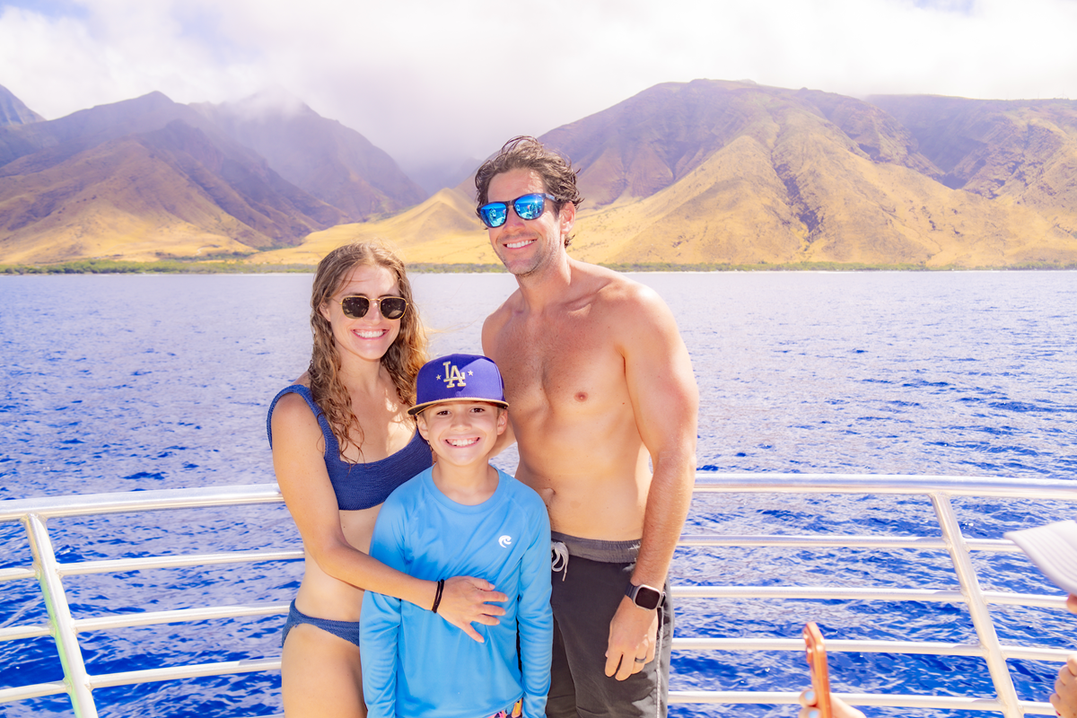 Family of three aboard a Maui snorkeling tour boat with the island coastline behind them