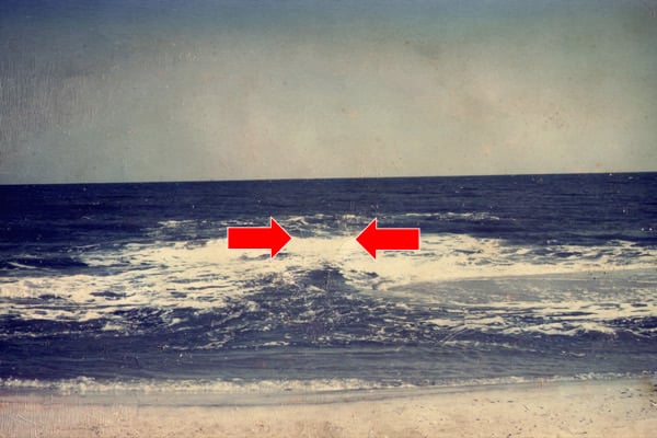 Beach-level view of a rip-current channel marked by red arrows between breaking waves